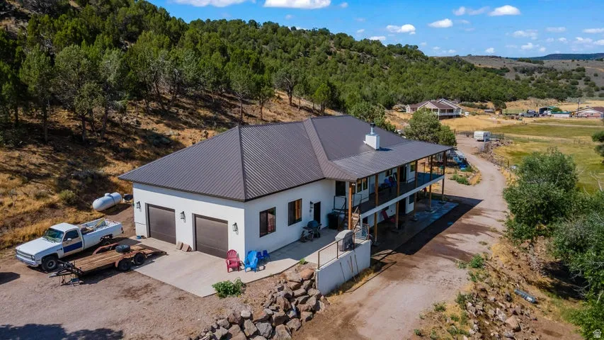 Contemporary residence featuring a two-car garage, a two-story wrap-around covered porch, and a dark metal roof