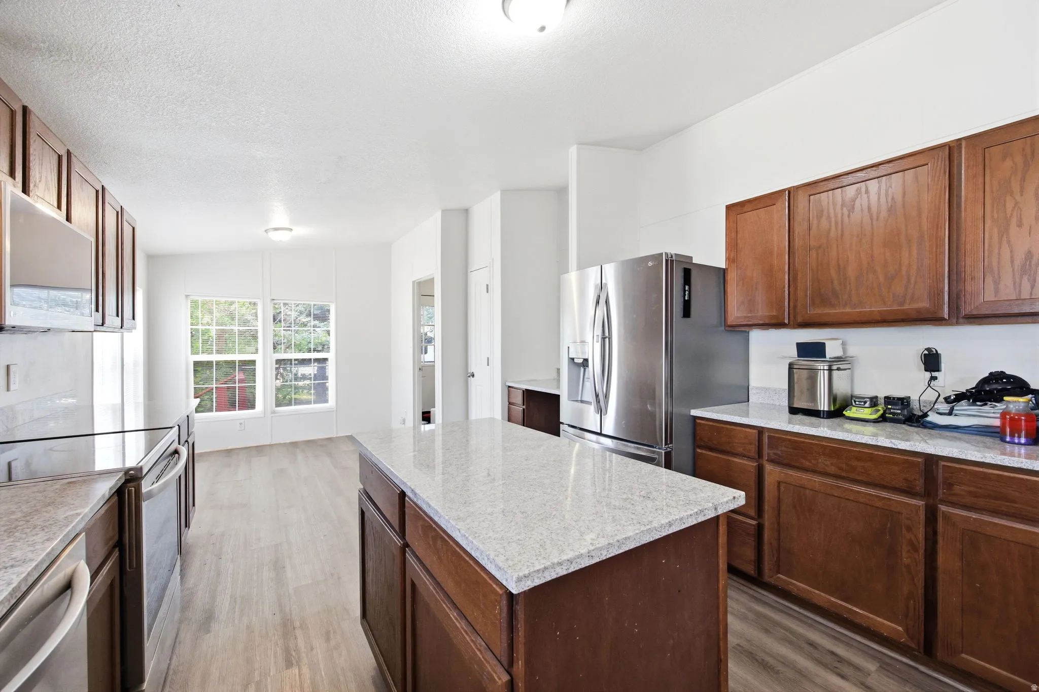 Kitchen featuring a central island with a light-colored countertop, wood-finish cabinetry, stainless steel appliances, light wood-finish flooring, and multiple windows