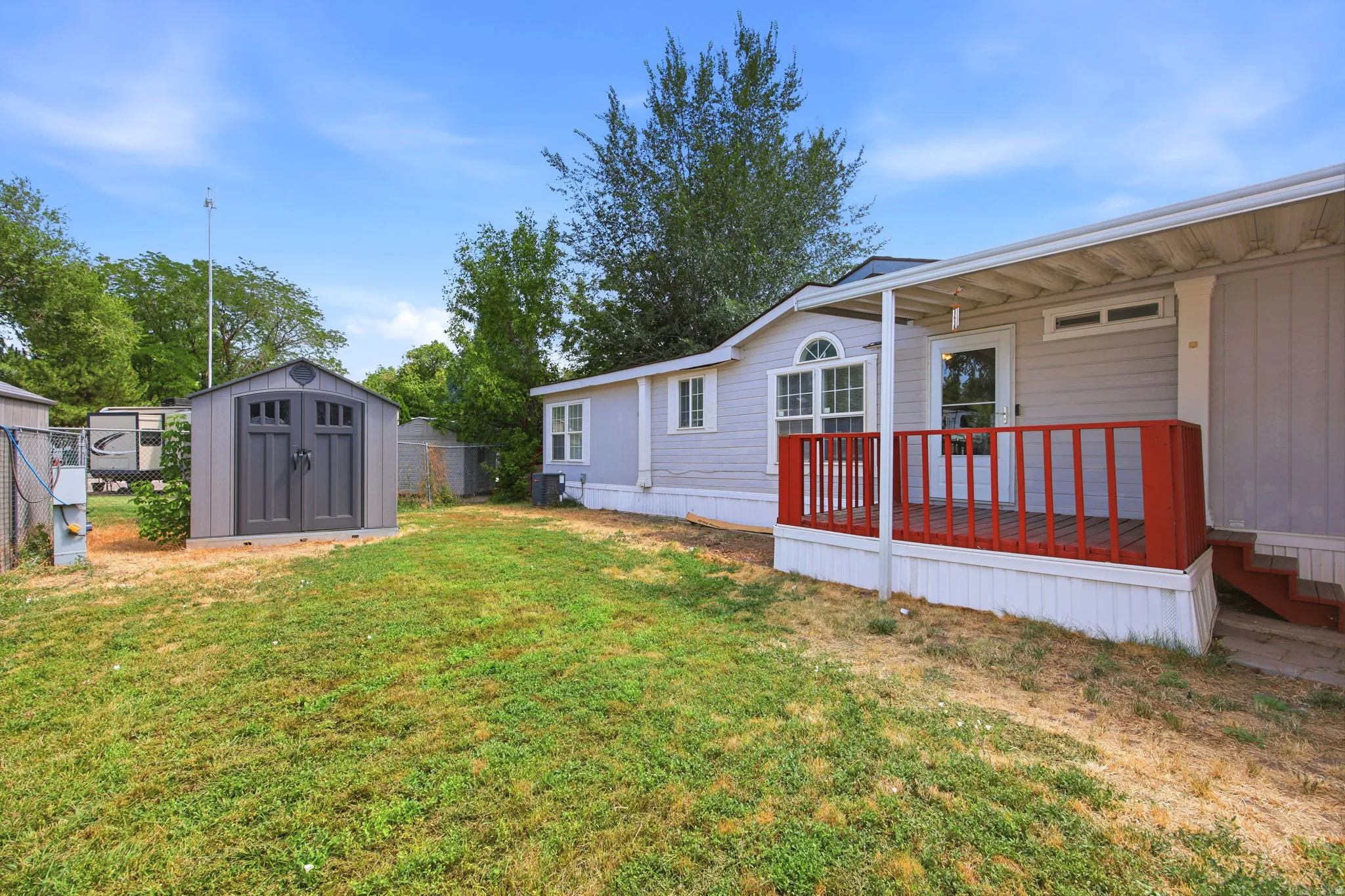 Exterior featuring a covered porch with red railings, light-colored siding, and a gabled storage shed