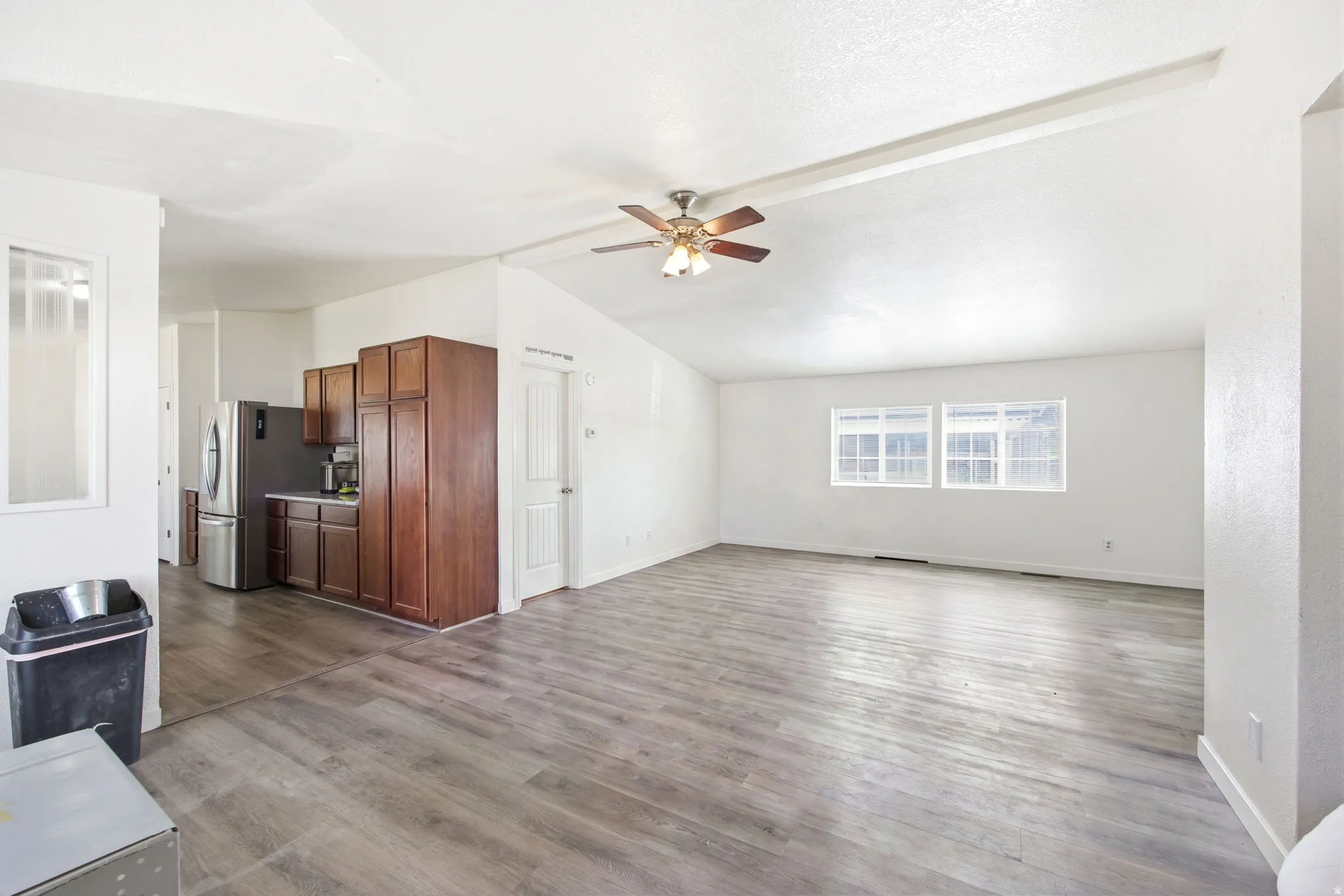 Open-concept living space featuring wood-finish flooring, vaulted ceilings, and a ceiling fan with integrated lighting