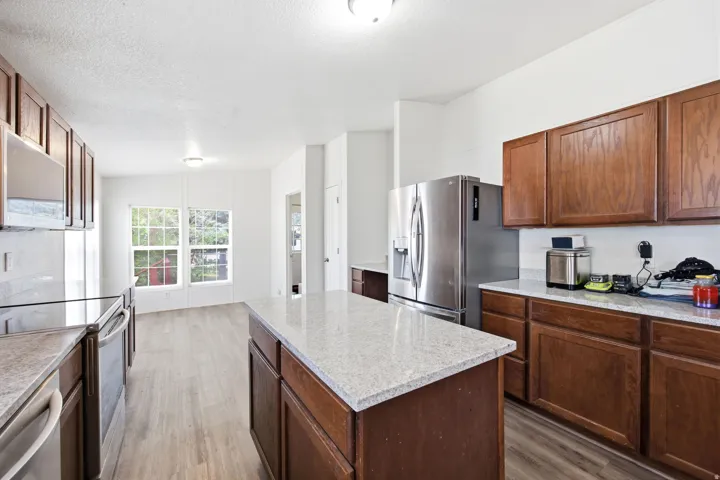 Kitchen featuring a central island with a light-colored countertop, wood-finish cabinetry, stainless steel appliances, light wood-finish flooring, and multiple windows