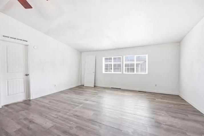 Spacious room featuring light wood-finish flooring, white walls, and multiple windows