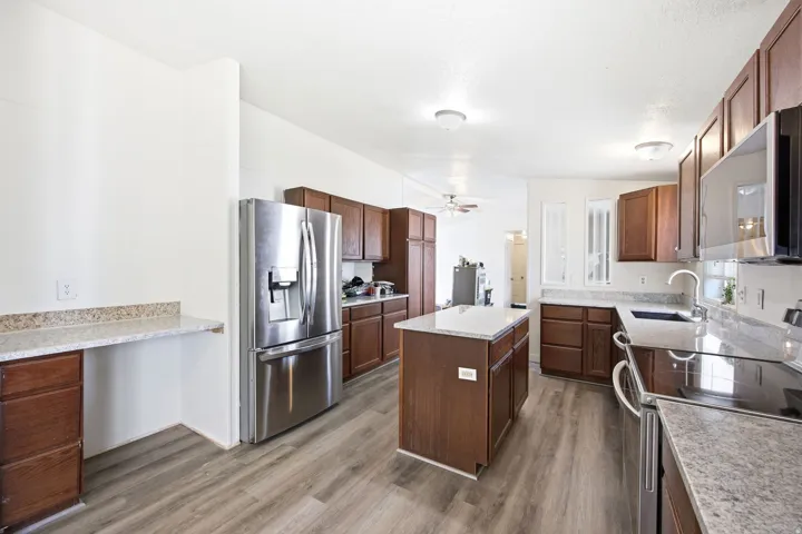 Kitchen featuring wood-finish flooring, dark wood cabinetry, light-toned countertops, a central island, and stainless steel appliances