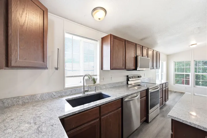 Kitchen featuring dark wood cabinetry, light-toned countertops, stainless steel appliances, and wood-finish flooring