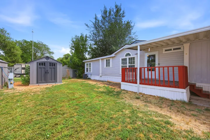Exterior featuring a covered porch with red railings, light-colored siding, and a gabled storage shed