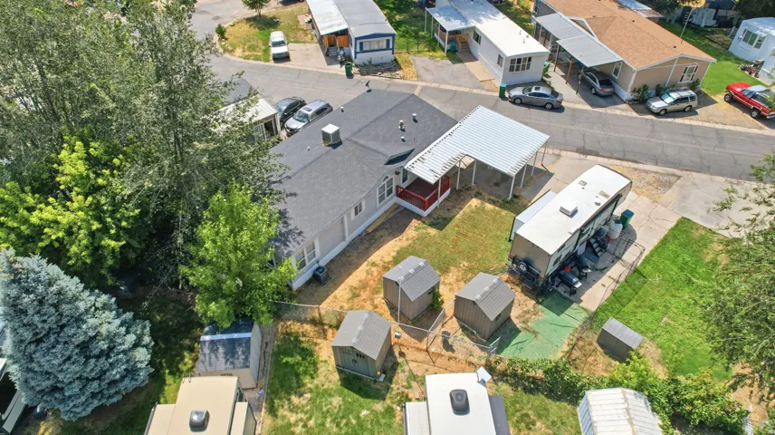 Aerial view of a property featuring a single-story residence with a dark shingled roof, an attached white carport, and a gravel driveway