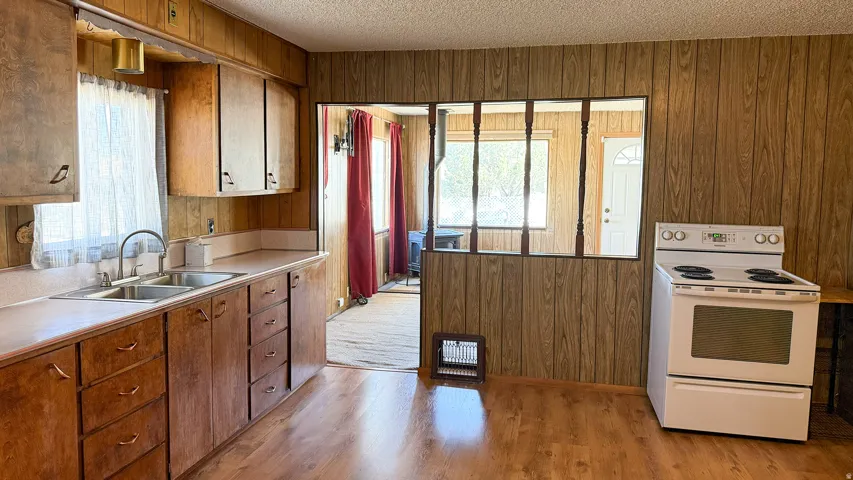 Kitchen featuring wood-finish flooring, wood-paneled walls, light wood cabinetry, a double basin stainless steel sink, and a white electric range