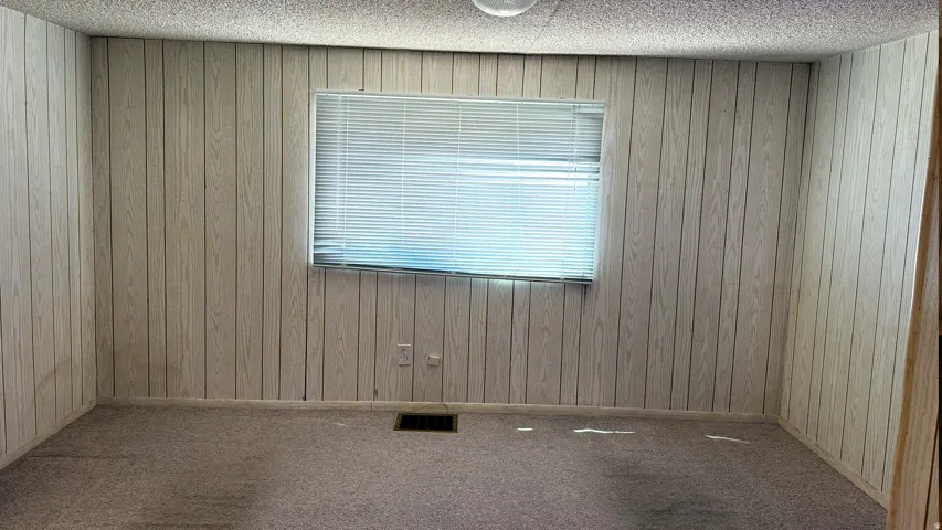 Interior room featuring light-toned wood-panel walls, a window with horizontal blinds, and carpet flooring