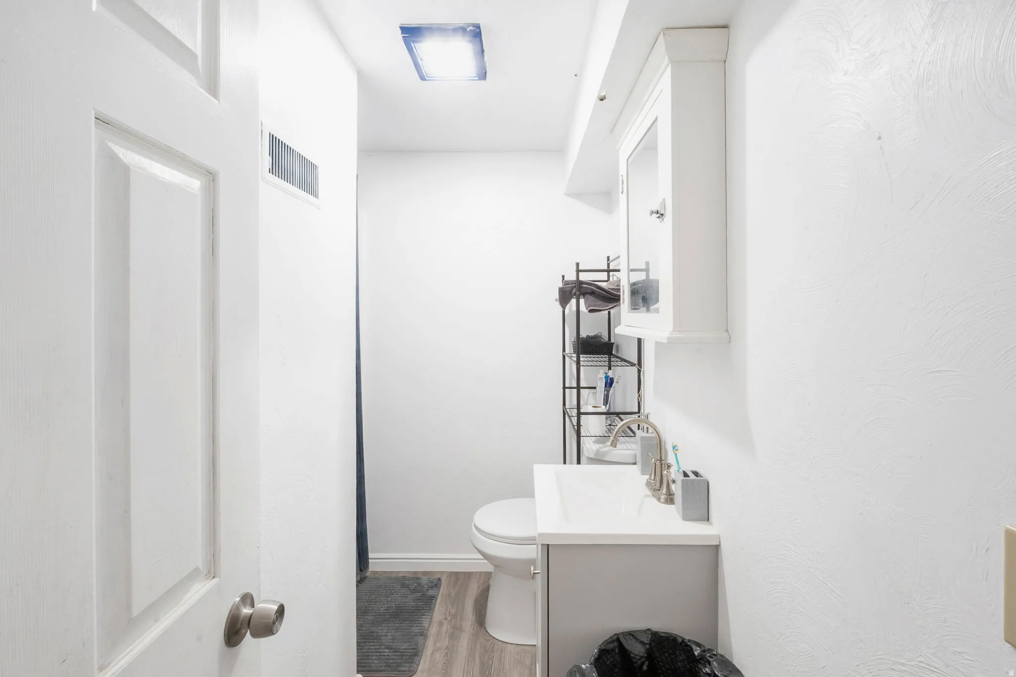 White painted door with brushed nickel hardware, light wood-finish flooring, and wall-mounted vanity with integrated sink