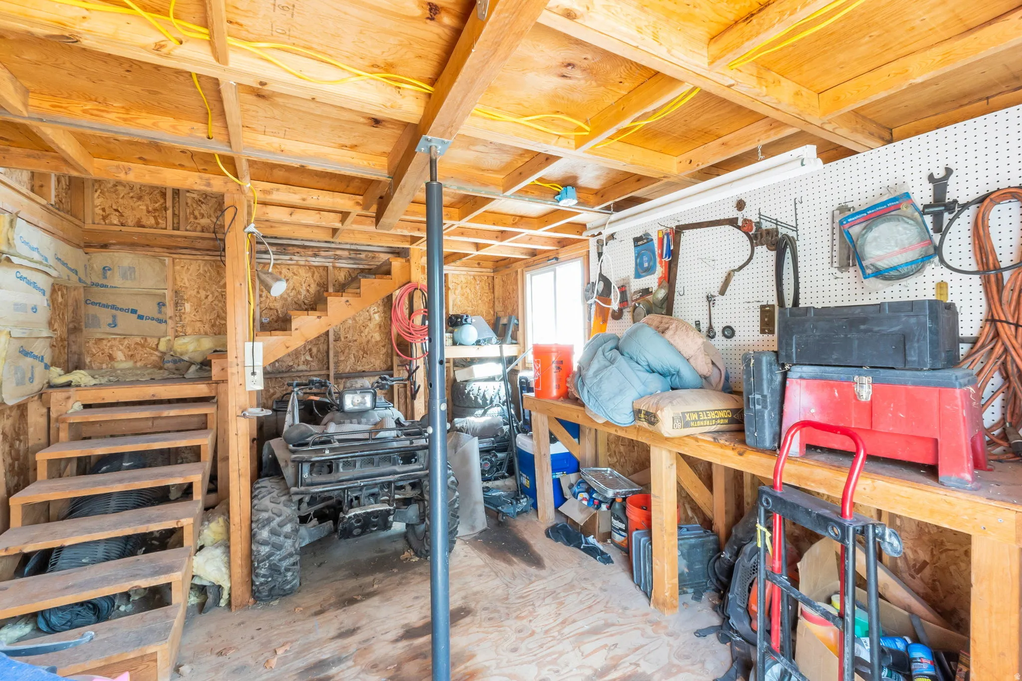 Unfinished utility space featuring exposed wood framing, an unfinished wood staircase, and a built-in workbench with pegboard organization