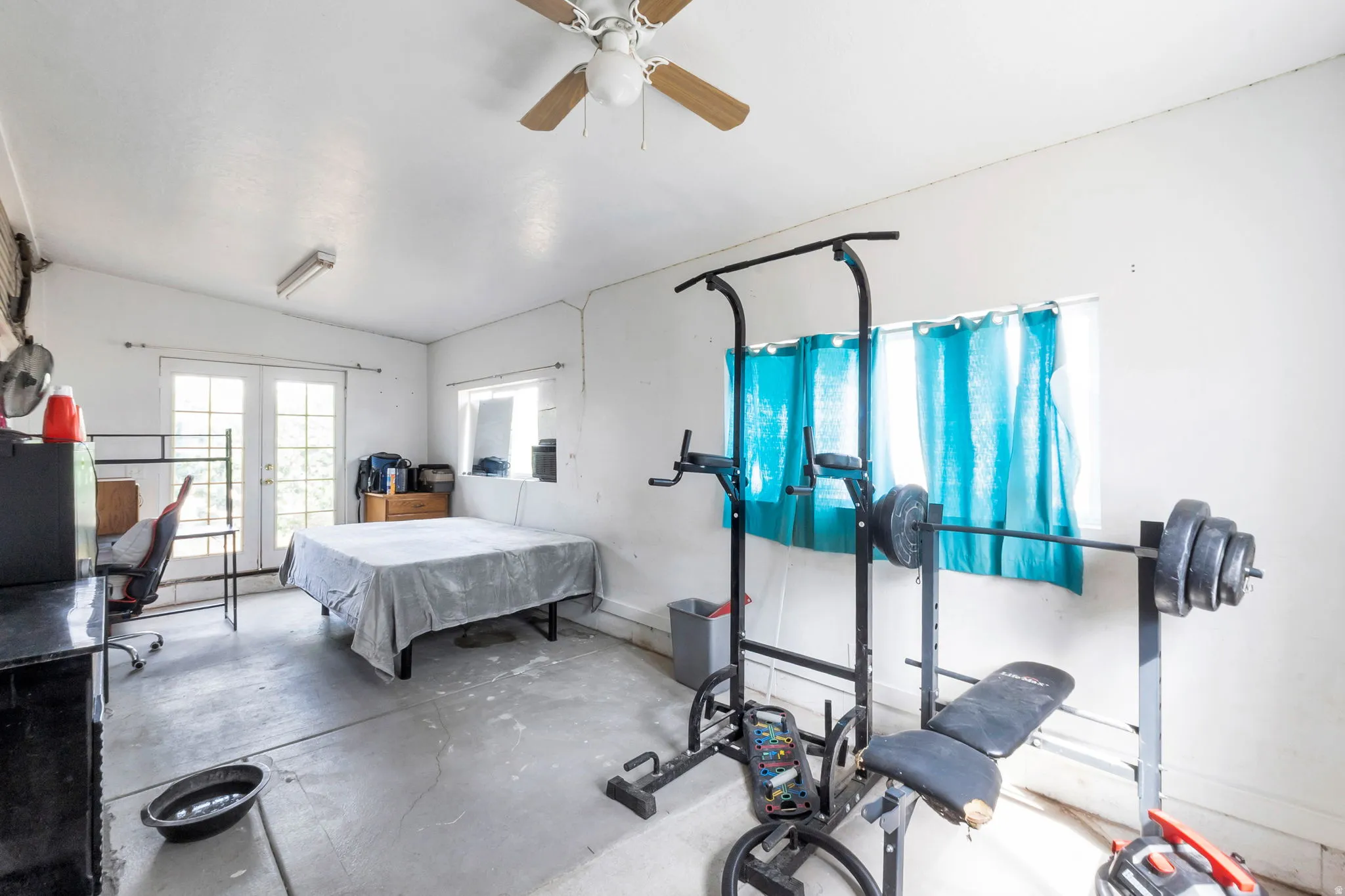 Spacious room featuring a ceiling fan, dual French doors, a window, and concrete flooring