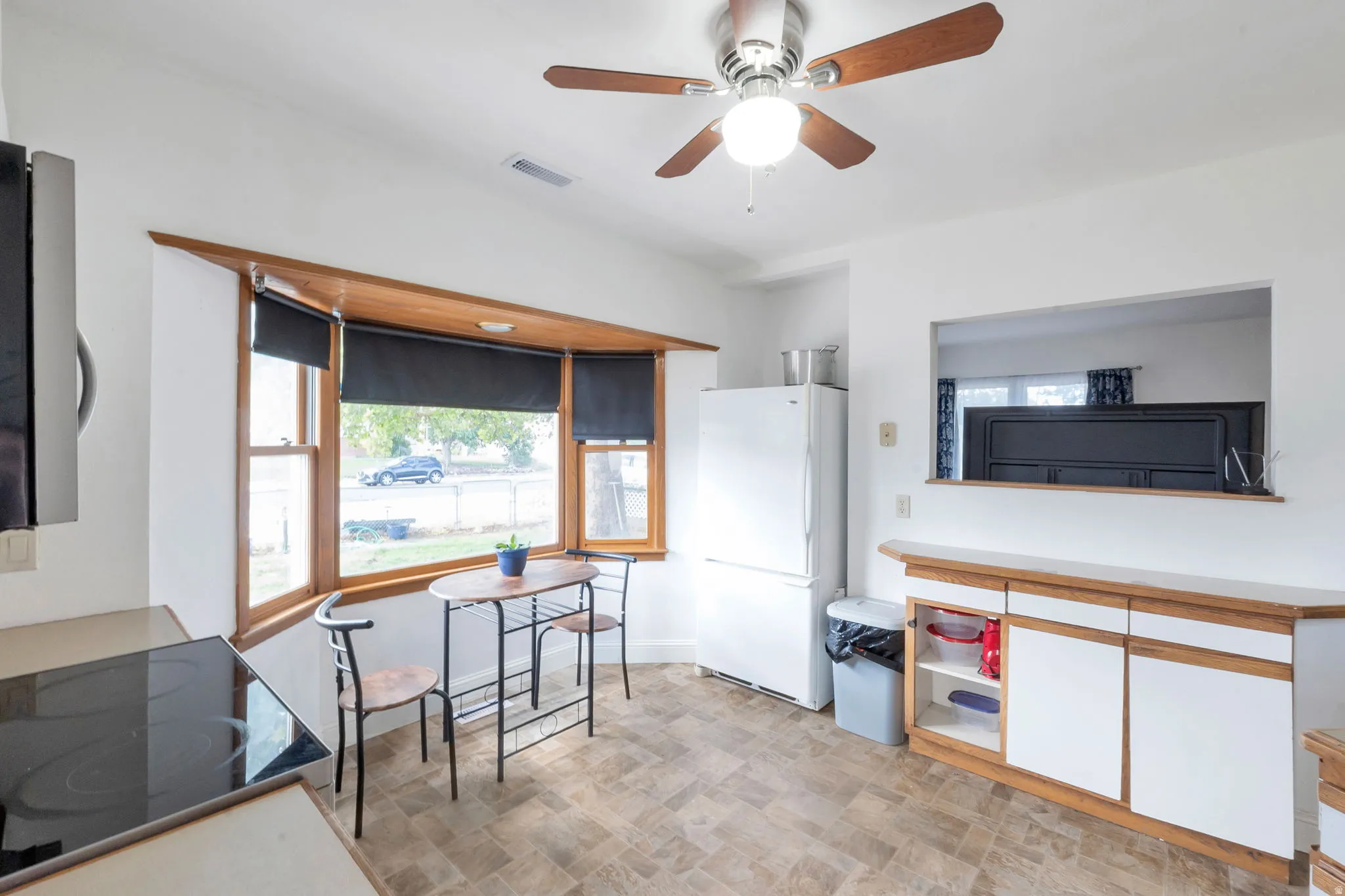 Kitchen featuring a bay window, ceiling fan, pass-through window, built-in cabinetry with white doors, and wood-finish trim