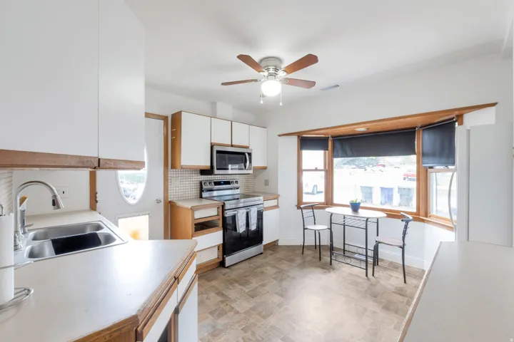 Functional kitchen featuring white cabinetry, light countertops, stainless steel appliances, a tile backsplash, and a bay window