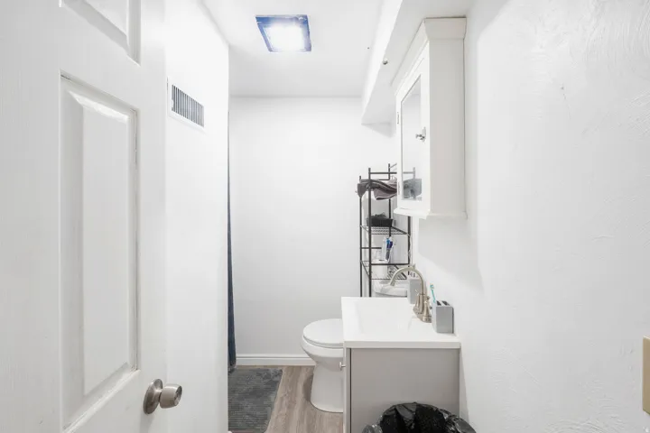 White painted door with brushed nickel hardware, light wood-finish flooring, and wall-mounted vanity with integrated sink