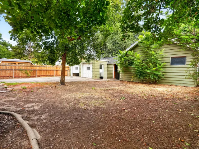 Rear exterior featuring horizontal siding, multiple mature trees, a detached two-car garage with white paneled doors, and a concrete driveway