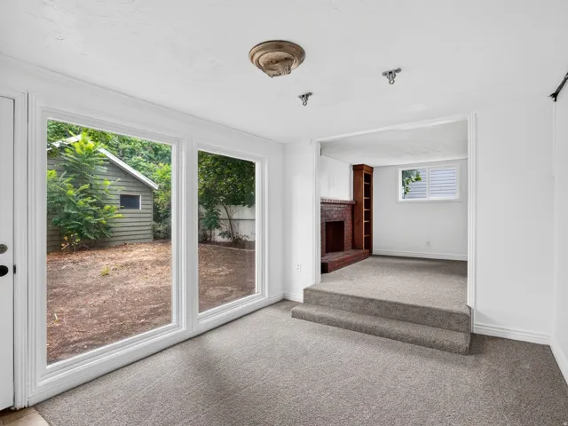 Spacious carpeted room featuring large windows overlooking the backyard, a multi-level transition to an additional living area, and a brick fireplace with built-in shelving