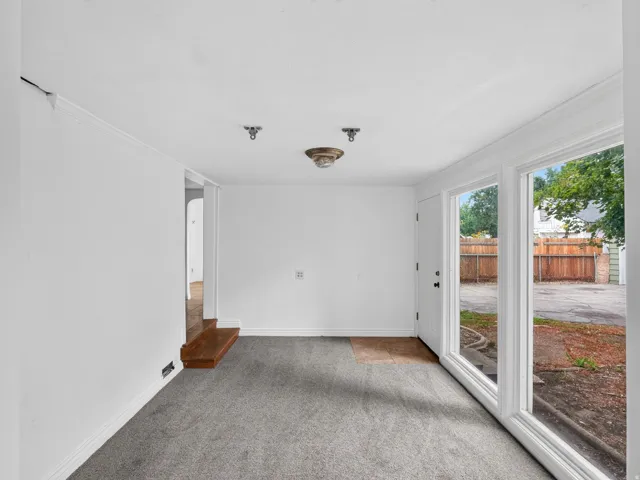 Room featuring light gray carpeting, a single white entry door, and a multi-pane window assembly
