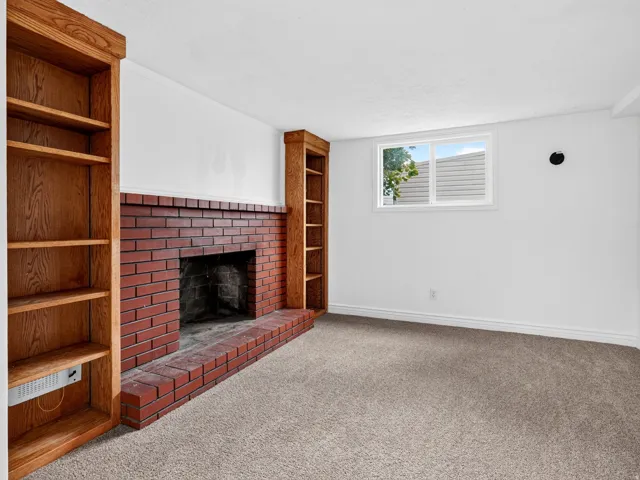 Living space featuring a brick fireplace with hearth, built-in wooden shelving, and soft gray carpeting