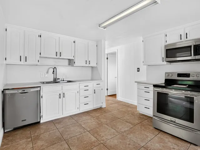 Kitchen featuring white cabinetry with black hardware, stainless steel appliances, and a tile floor