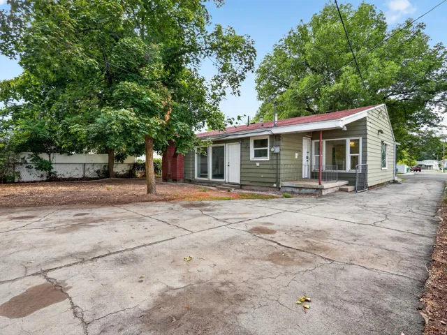 Green siding exterior with a red roof, featuring a concrete driveway and mature trees