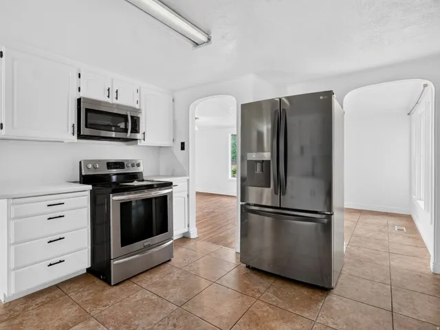 Kitchen featuring stainless steel appliances, white cabinetry with dark hardware, a tile floor, and an arched doorway