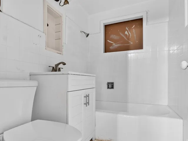 White tiled bathroom featuring a built-in bathtub, a white vanity with cabinet storage, and a polished chrome faucet