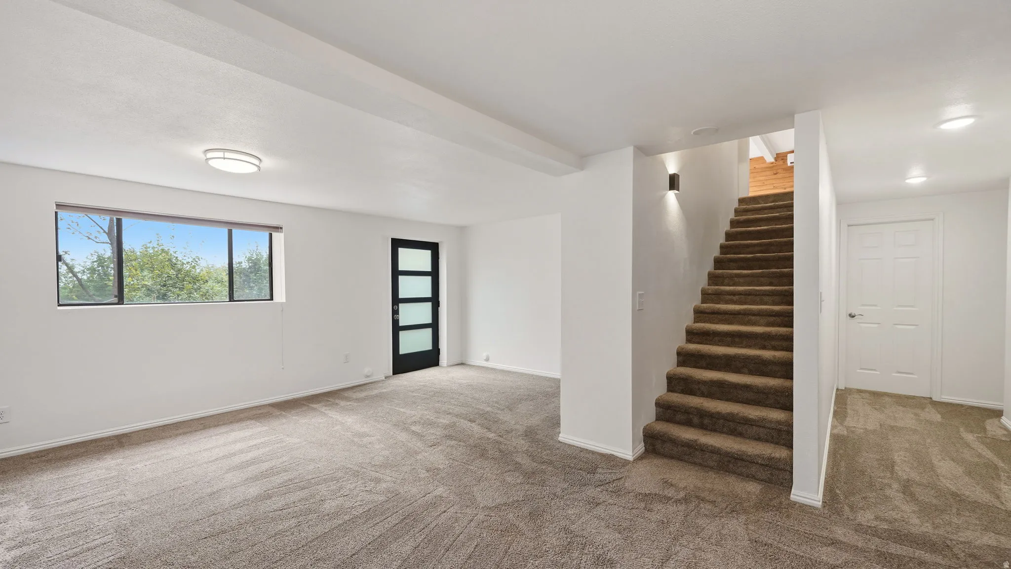 Spacious room featuring neutral carpeting, recessed lighting, a modern black door with frosted glass panels, and a large window providing ample natural light