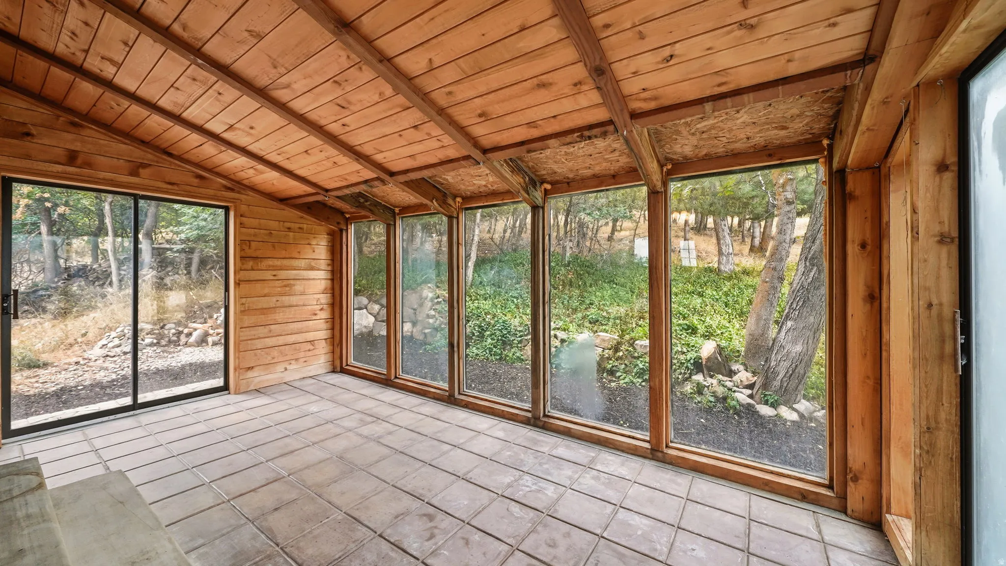 Enclosed patio featuring a wood-paneled ceiling, wood-plank walls, tiled flooring, expansive windows, and a sliding glass door