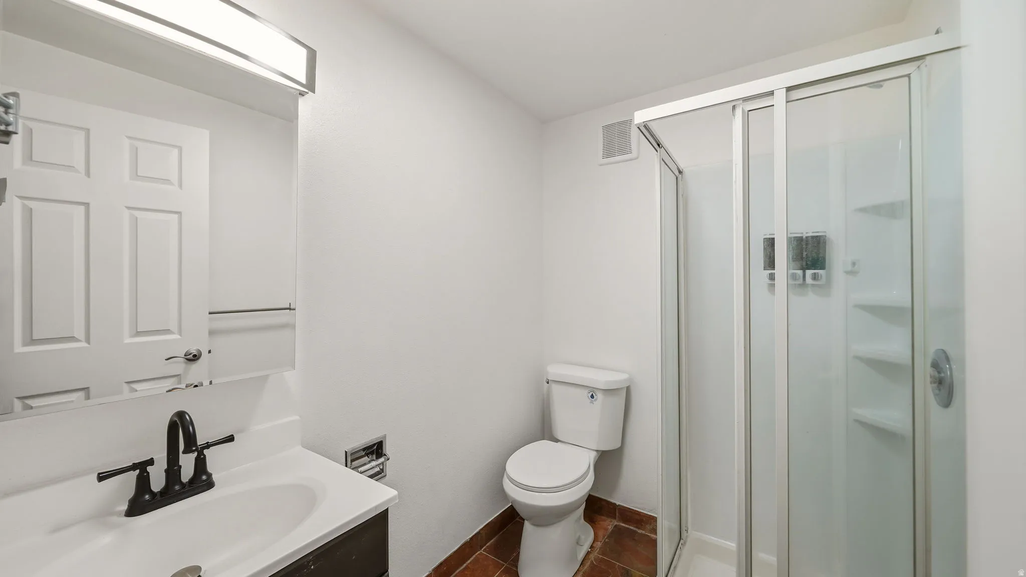 Bathroom featuring a vanity with a white countertop and black faucet, a toilet, and a stand-up shower with a sliding glass door