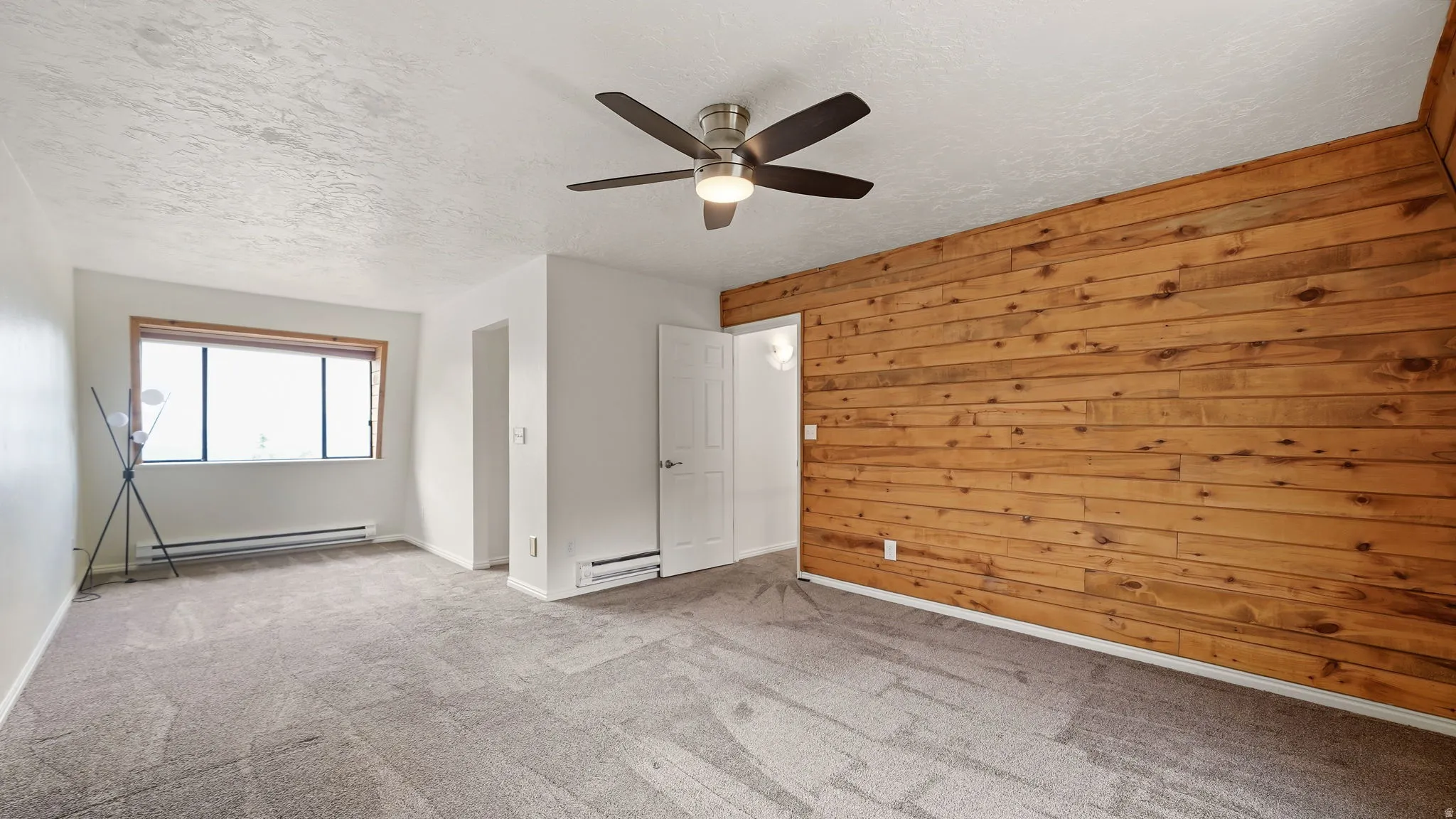 Spacious room featuring a prominent wood panel accent wall and light gray carpeting