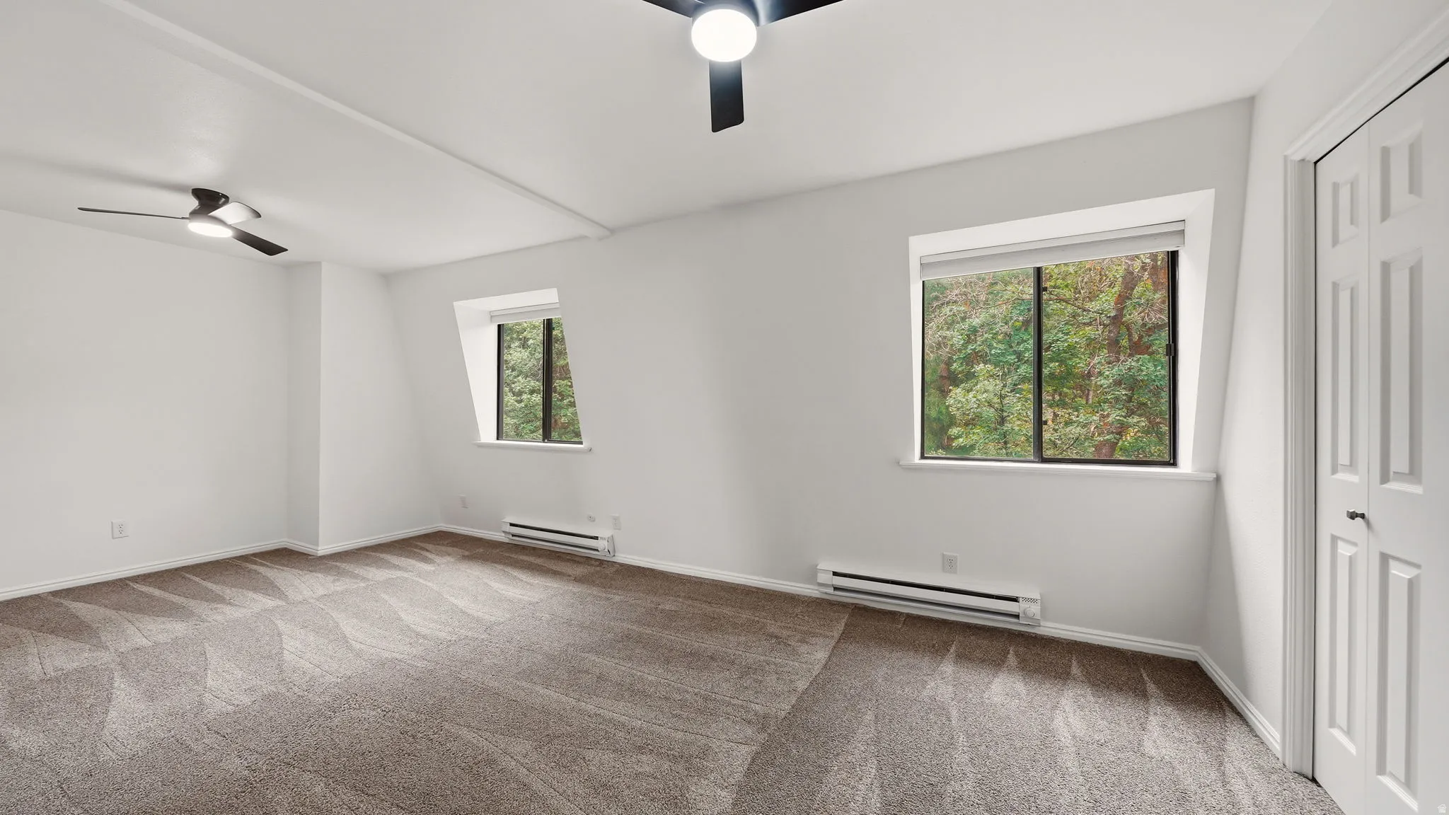 Spacious room featuring patterned carpeting, two windows, two ceiling fans, and baseboard heating