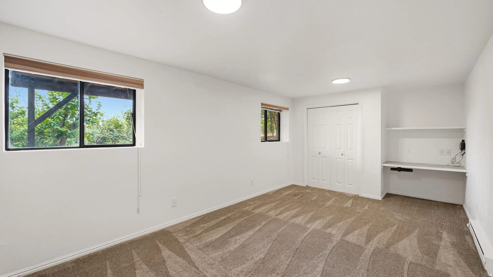 Carpeted room featuring multiple windows, a bi-fold closet, and a built-in desk with shelving