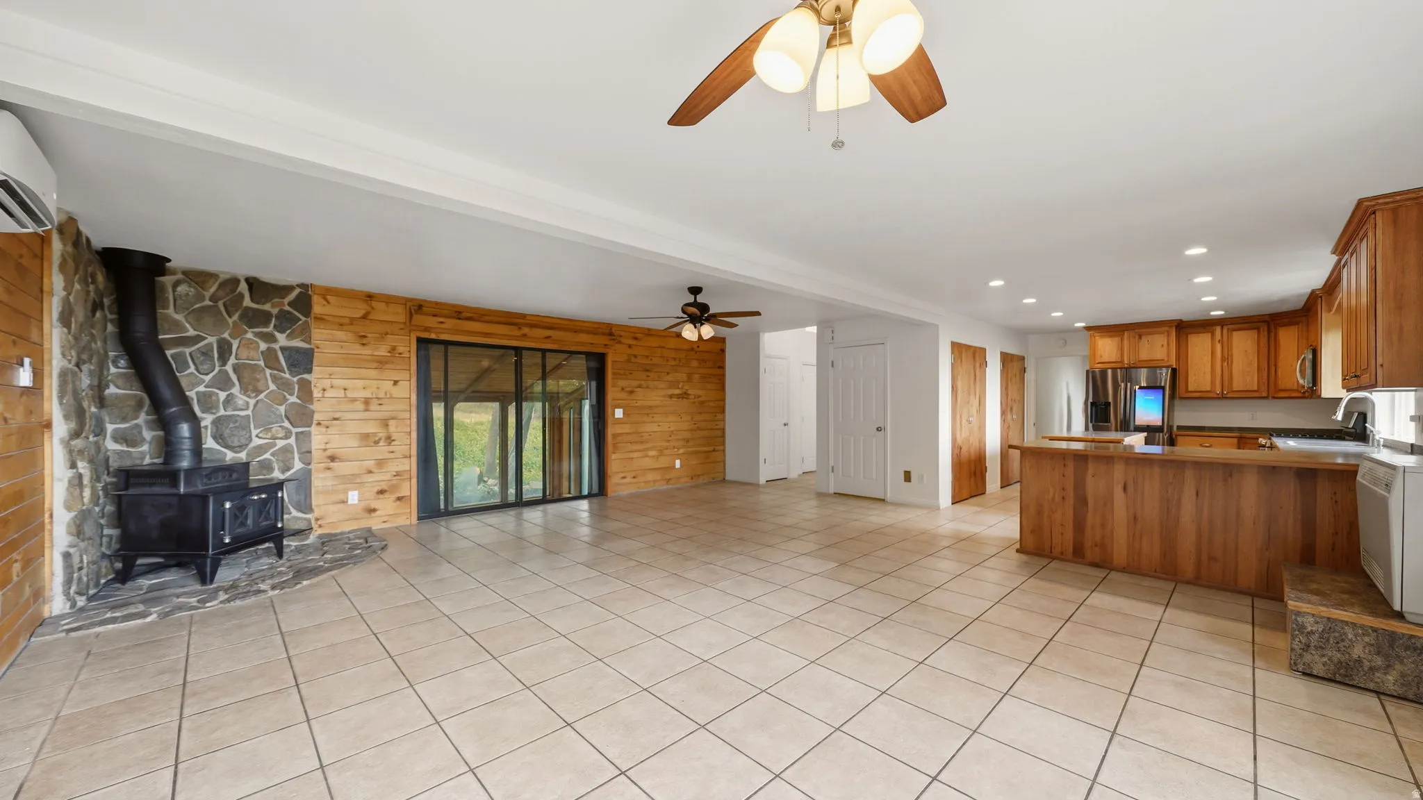 Open-concept living space featuring wood-finish flooring, a stone-clad fireplace wall with a wood-burning stove, and a full kitchen with wood cabinetry