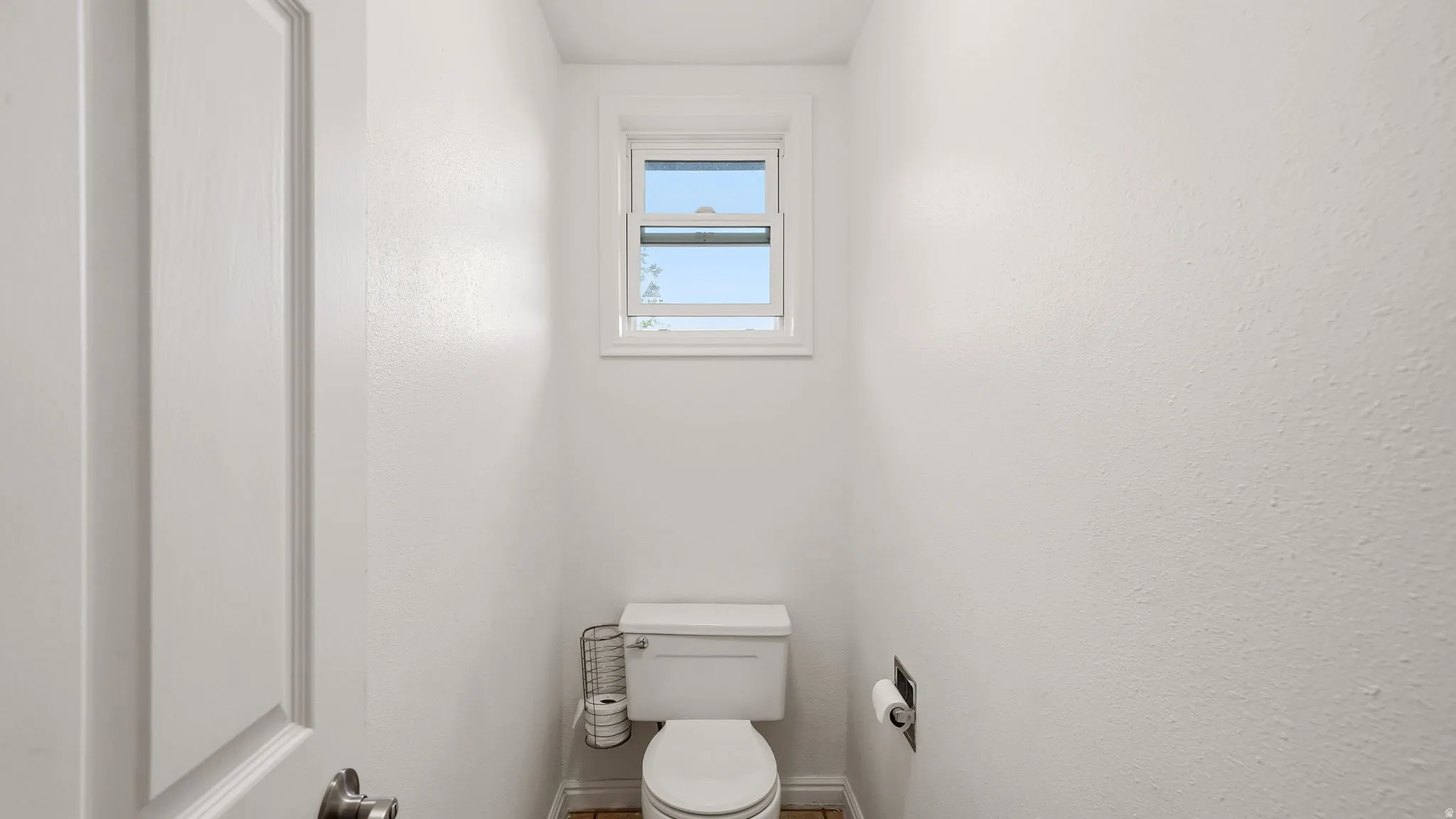 Powder room featuring a single toilet, a paneled door, and a window with natural light