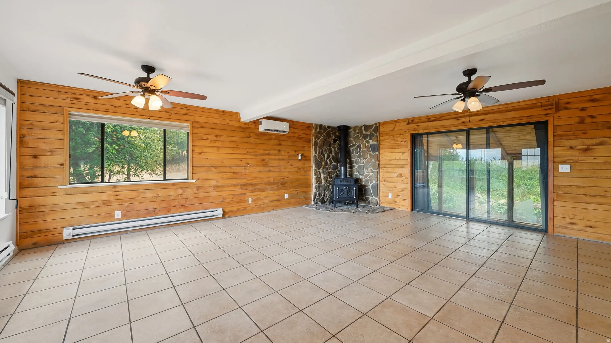 Spacious room featuring tile flooring, horizontal wood paneling, and a stone-clad hearth with a wood-burning stove