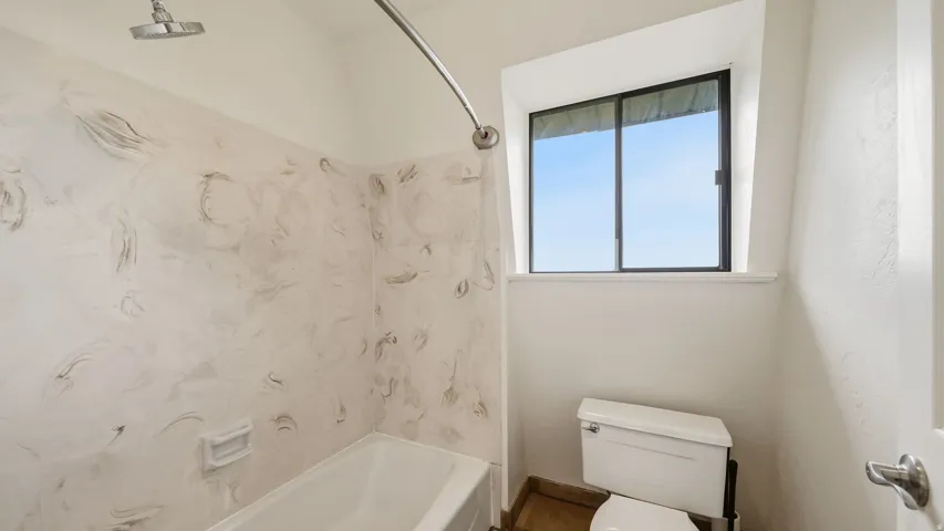 Bathroom featuring a white bathtub, patterned shower surround, and a window with natural light
