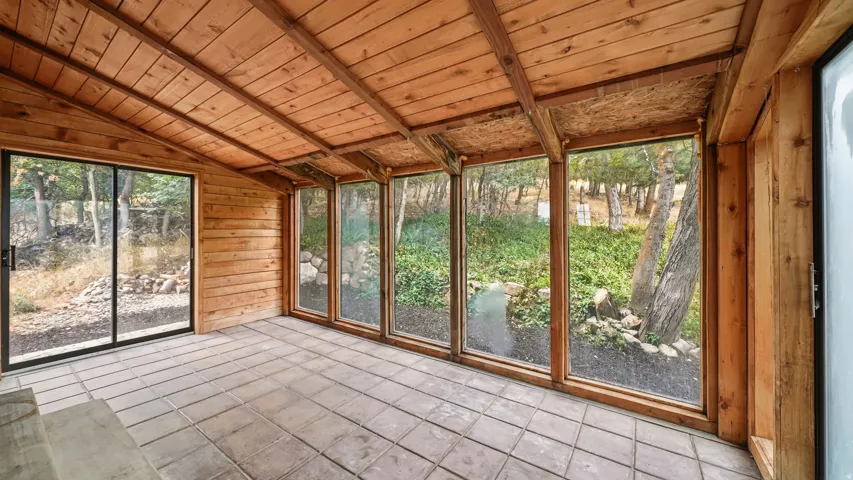Enclosed patio featuring a wood-paneled ceiling, wood-plank walls, tiled flooring, expansive windows, and a sliding glass door