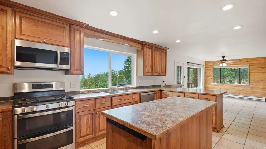 Spacious kitchen featuring wood cabinetry, stainless steel appliances, a center island with a stone-look countertop, and recessed lighting