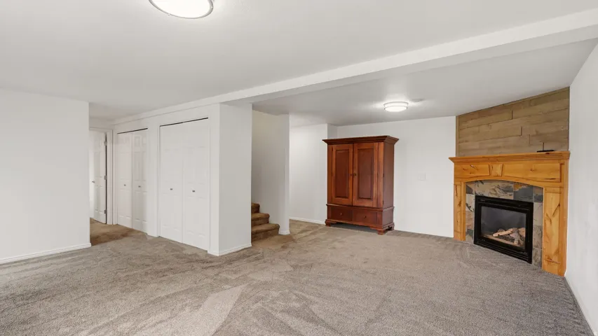 Spacious room featuring neutral carpeting, a built-in fireplace with a stone surround and wood mantel, and multiple bi-fold closet doors