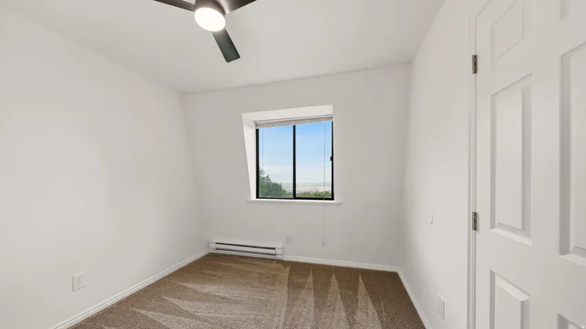 Bright room featuring a window with a distant landscape, neutral-toned carpet, white baseboards, and a ceiling fan