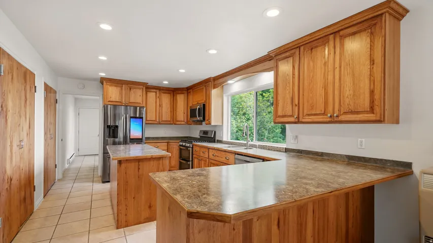 U-shaped kitchen featuring wood cabinetry, stainless steel appliances, and a central island with a contrasting countertop