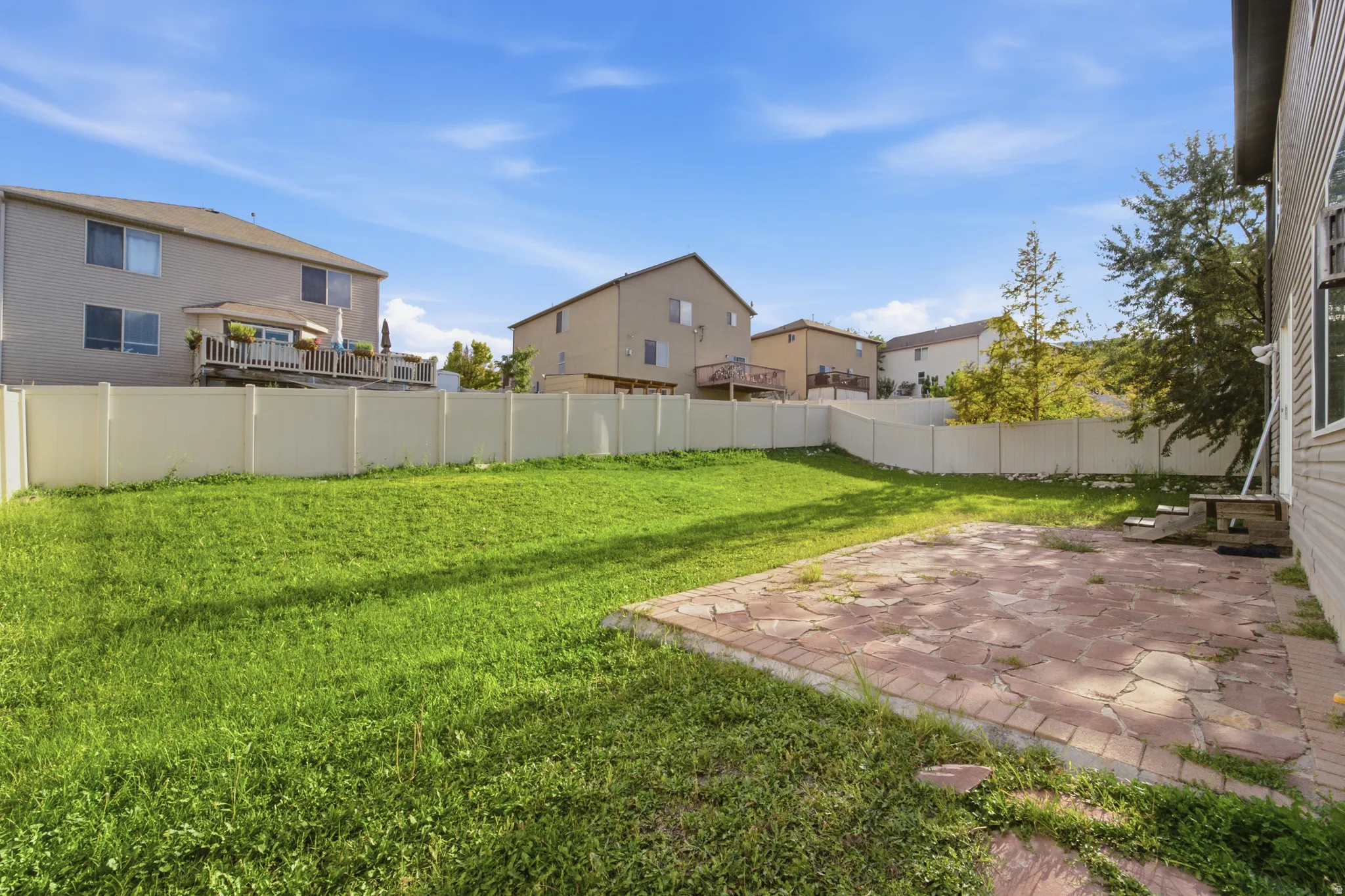 Expansive outdoor space featuring a large lawn area, a stone patio, and perimeter fencing