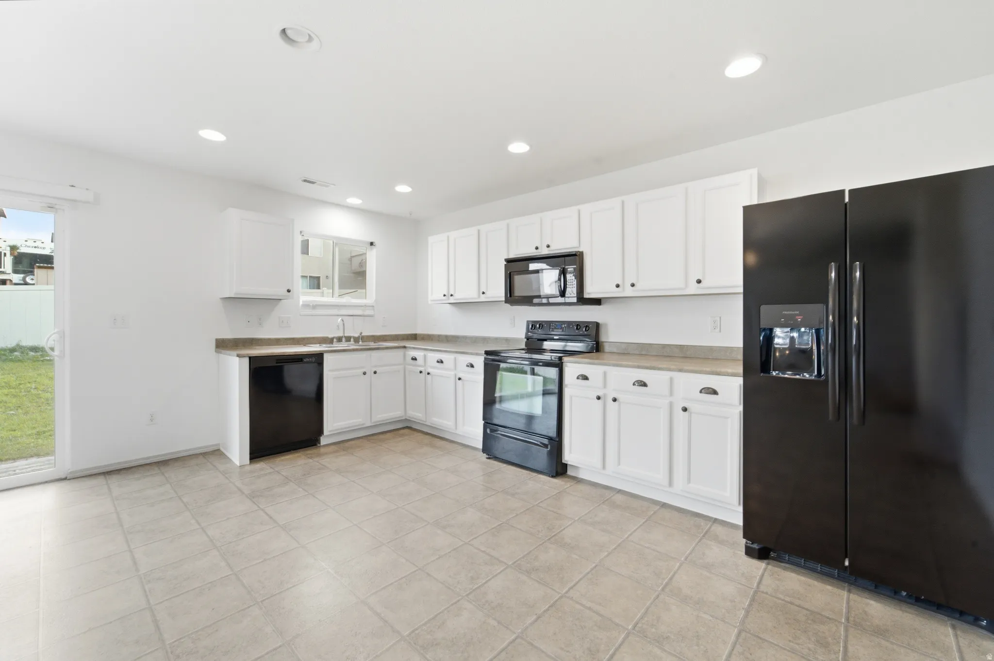 Spacious kitchen featuring white cabinetry, stainless steel appliances including a side-by-side refrigerator and double wall ovens, tile flooring, and an L-shaped layout with ample counter space and storage throughout