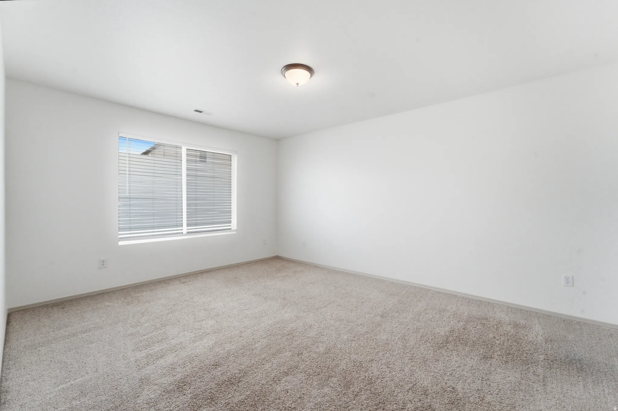 Expansive room featuring light-toned carpet, white walls, and a large window with horizontal blinds