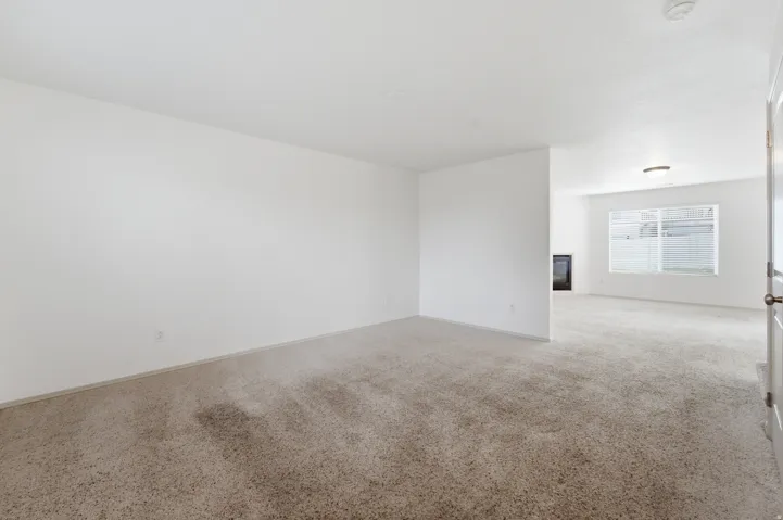 Expansive room with neutral carpeting, white walls, and a visible window, featuring a built-in fireplace and overhead lighting