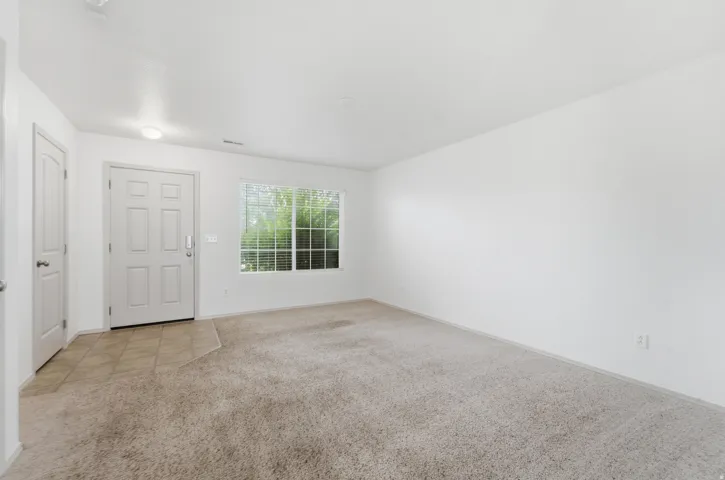 White paneled front door, tile flooring, window with blinds, and neutral carpeting