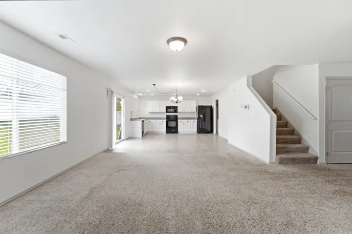Open-concept living space with light-toned carpeting and white walls