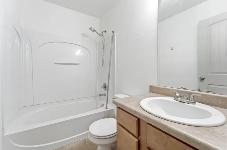 Bright, modern bathroom featuring a wood-finish vanity with an oval white porcelain sink, neutral stone-finish countertop, and chrome faucet