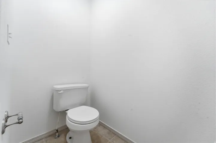 White toilet with a round bowl, tile flooring, and a brushed nickel toilet paper holder