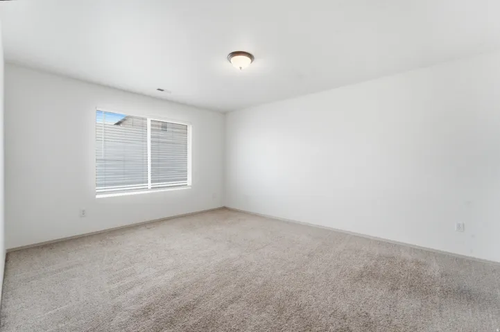 Expansive room featuring light-toned carpet, white walls, and a large window with horizontal blinds